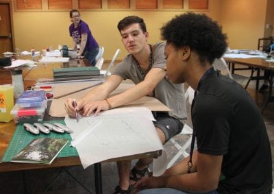 Fay Jones School student Beau Burris shows a Design Camp student how to finish the next step in her project. 